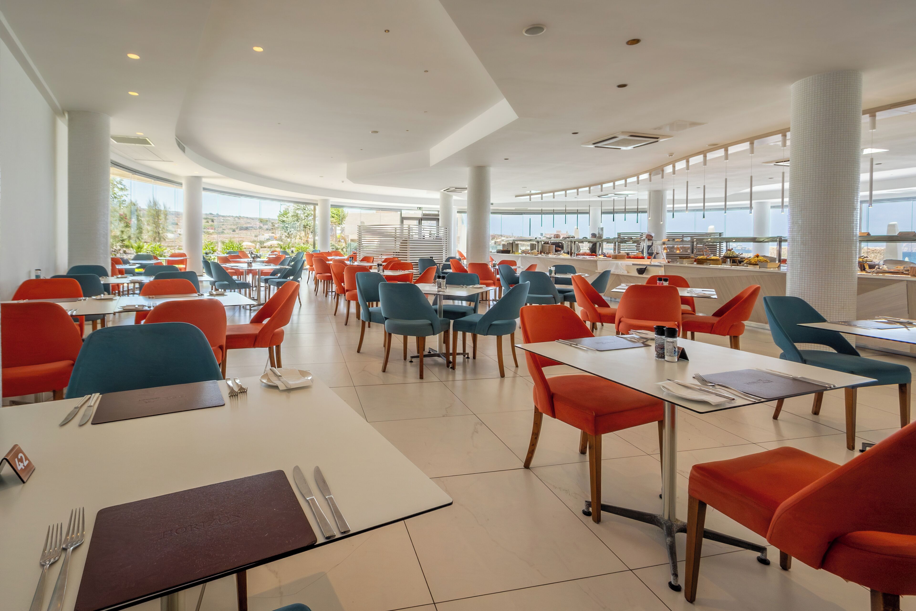 Un comedor amplio con mesas y sillas, ventanas grandes y vistas al exterior.
