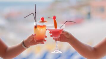 Two hands holding cocktail glasses with straws and cherries.