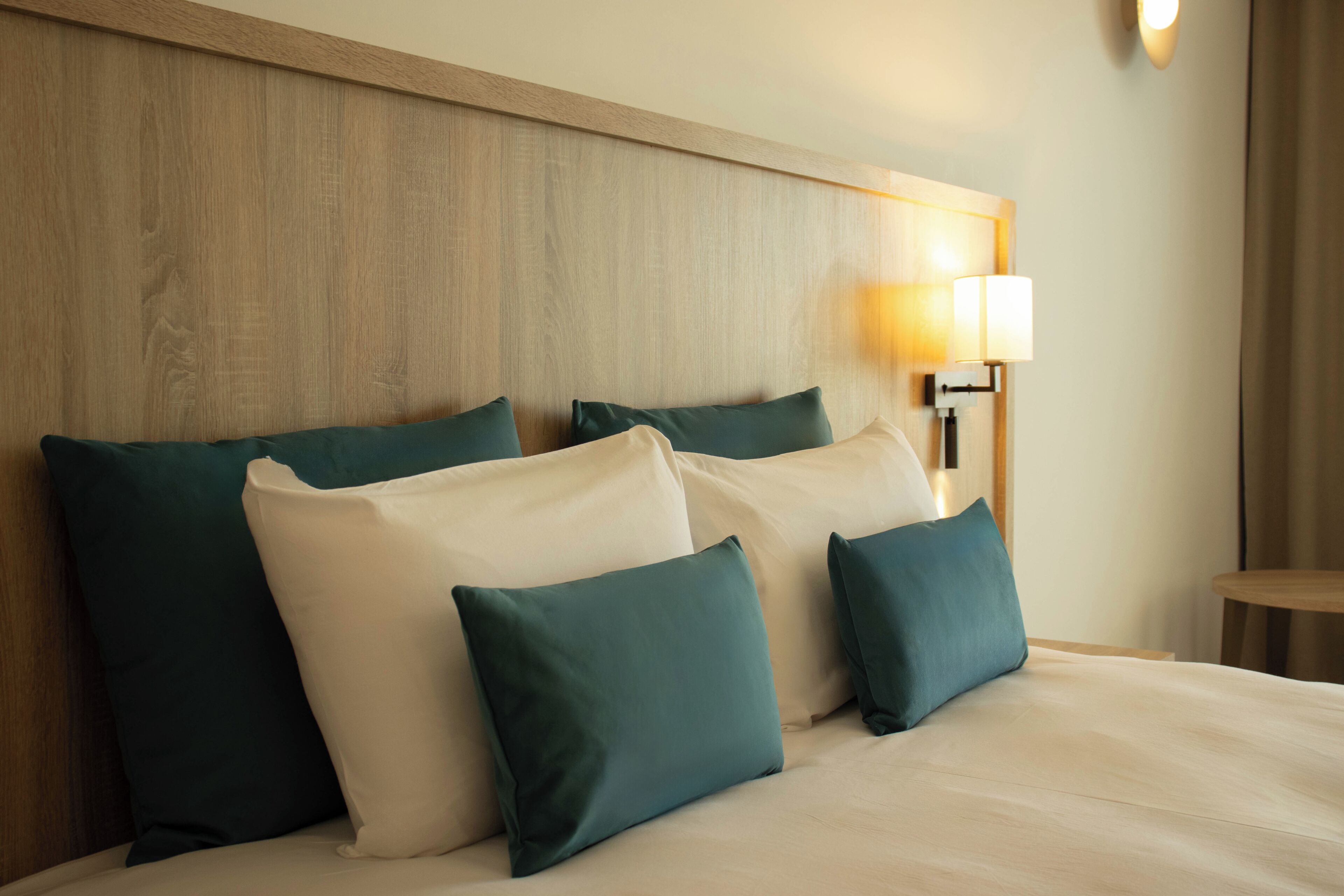 A bed with four pillows, a wooden headboard, and a bedside lamp.