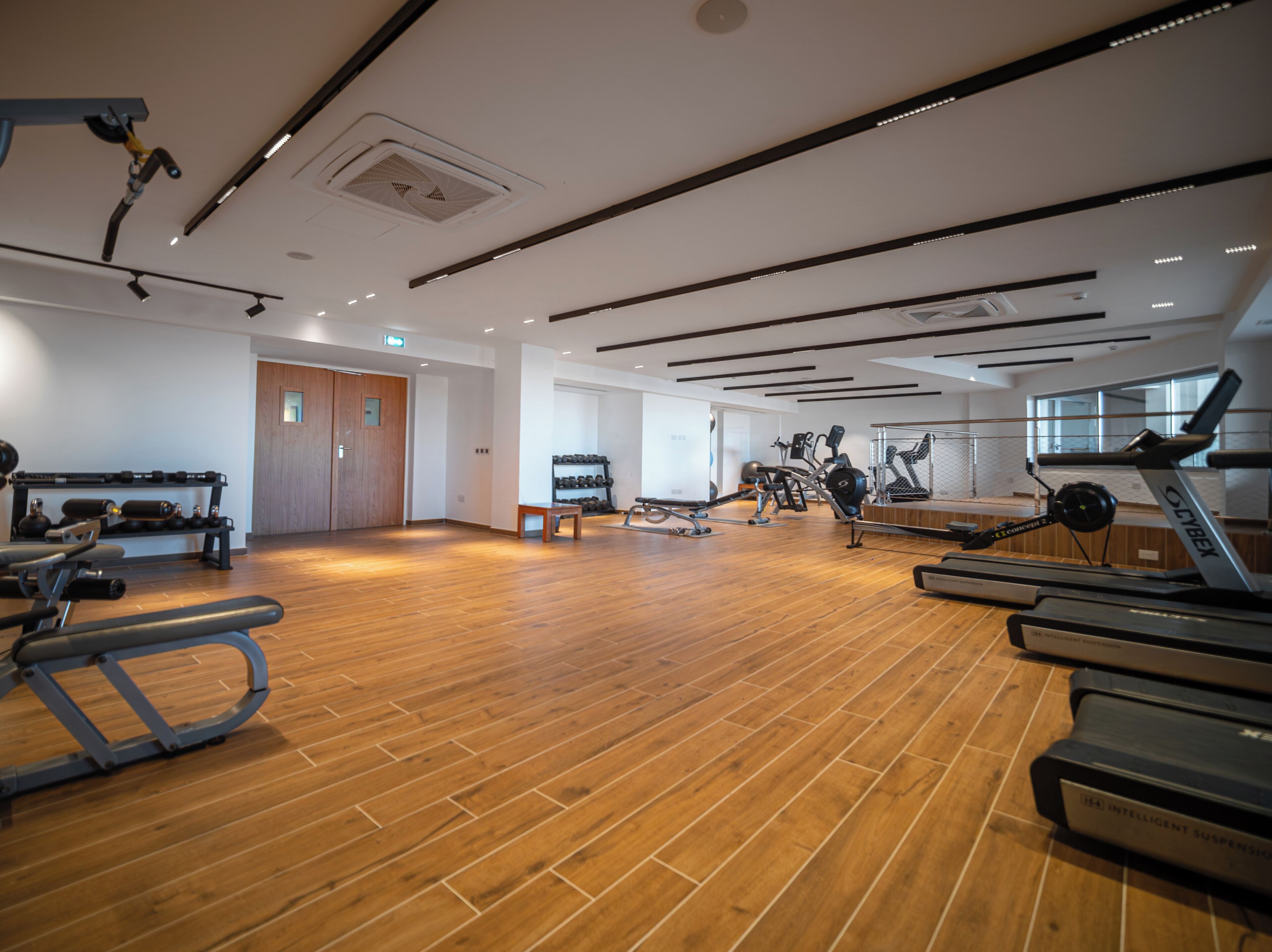 A gym with exercise equipment, wooden flooring, and a large mirror.