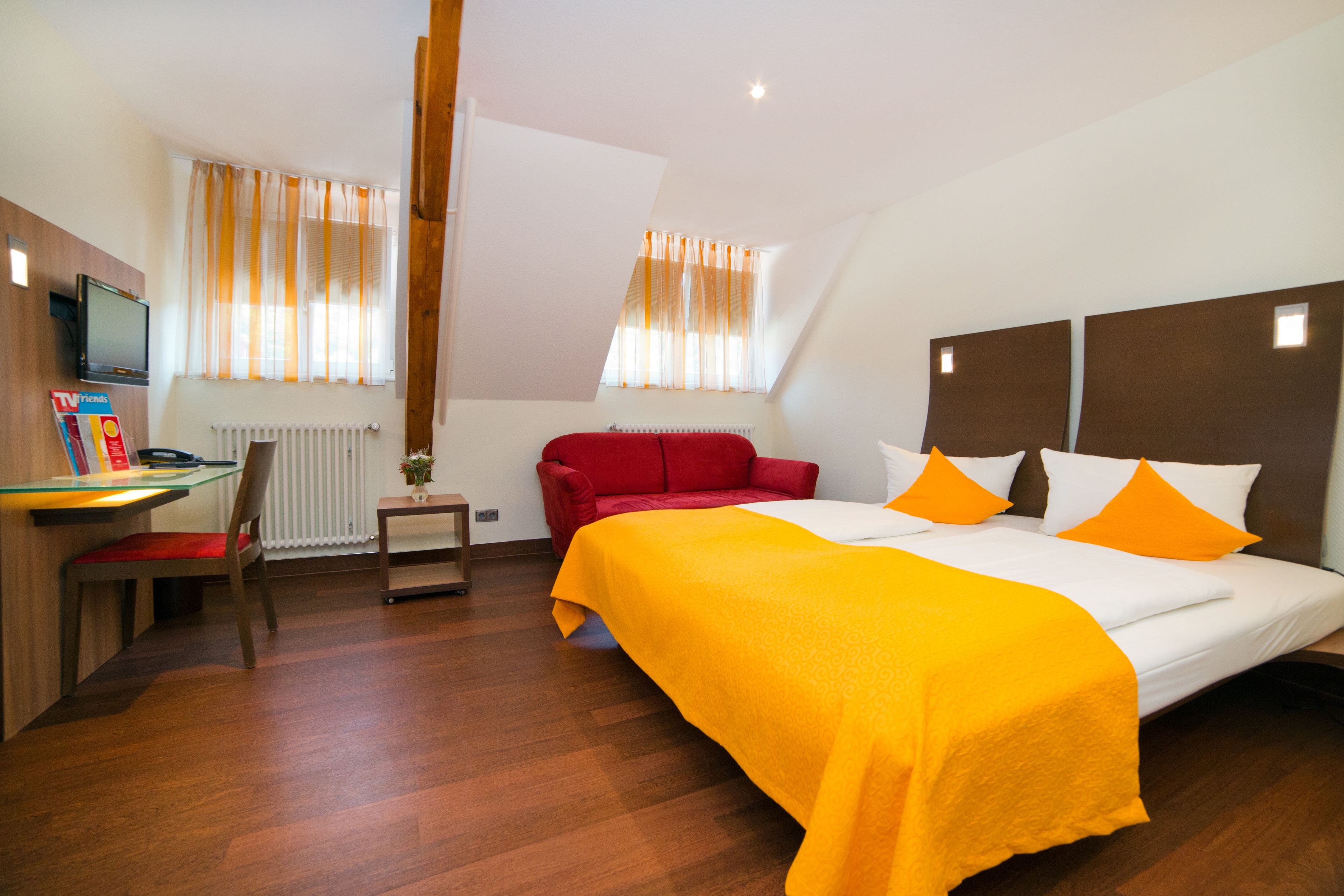 Habitación de hotel con cama, escritorio, silla, sofá rojo y televisor.