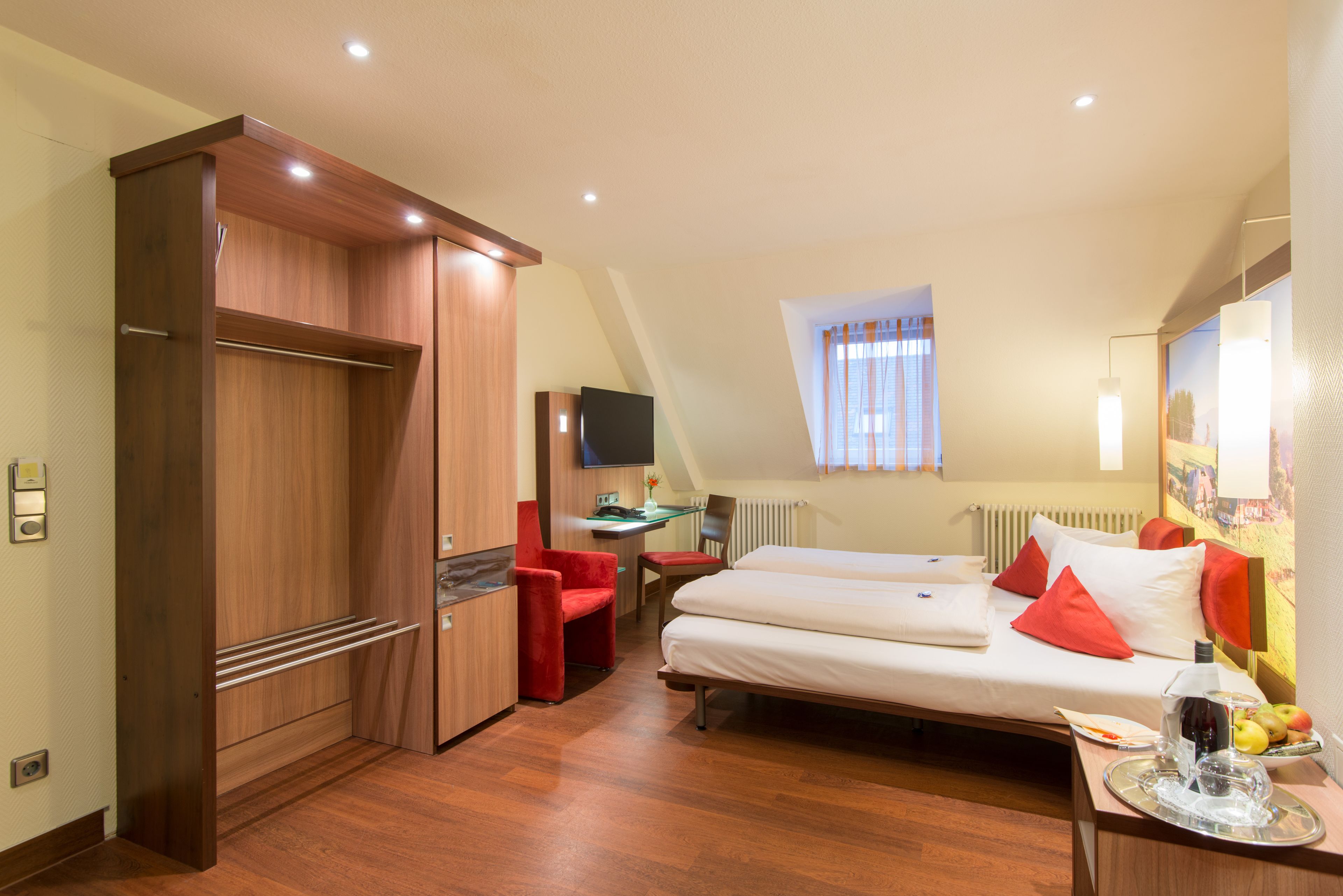 A hotel room with a bed, a desk, a chair, a TV, and a wardrobe.