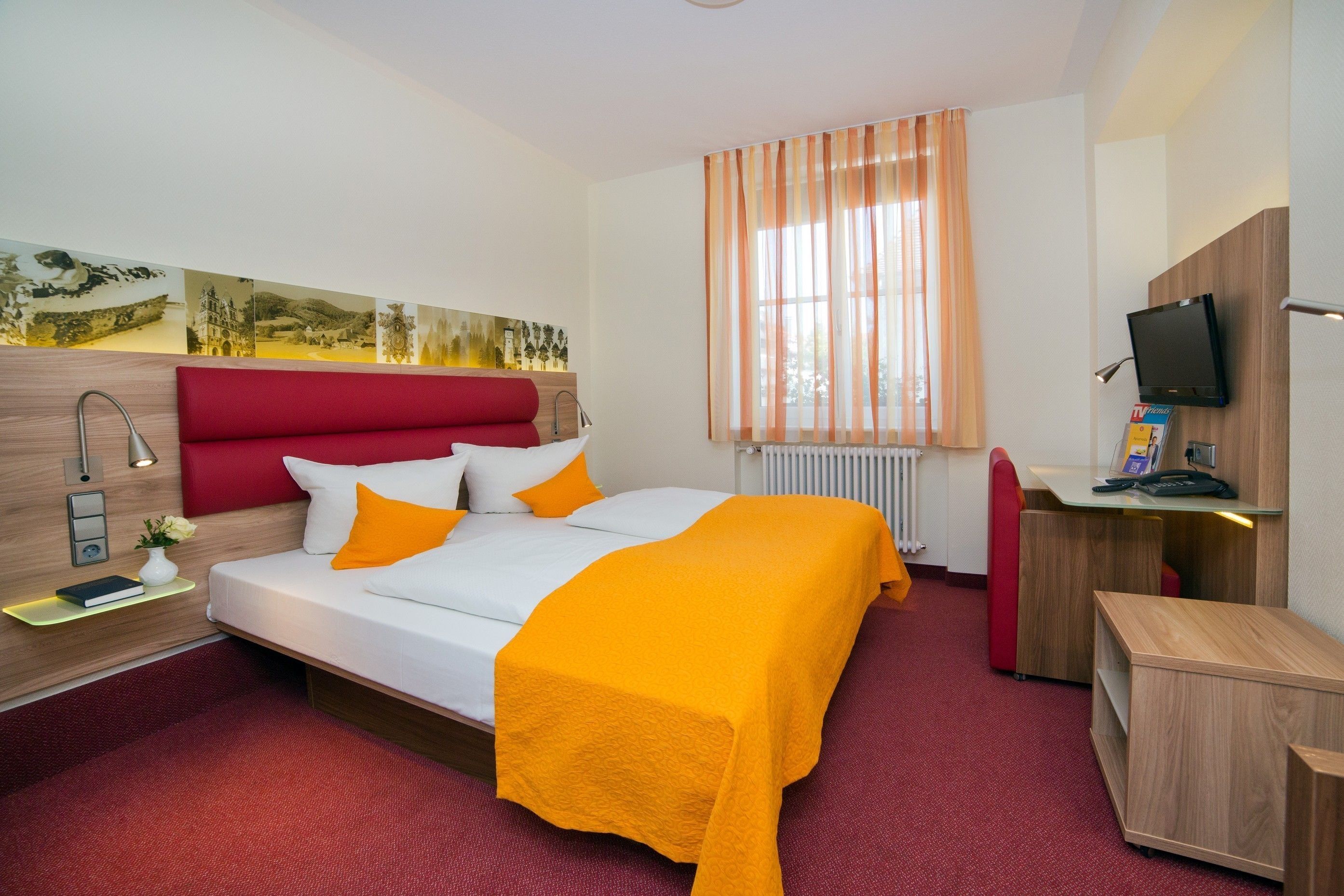 A hotel room with a bed, a desk, a TV, and a window with curtains.