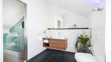 A modern bathroom with a white toilet, a wooden vanity, a large mirror, and a potted plant.