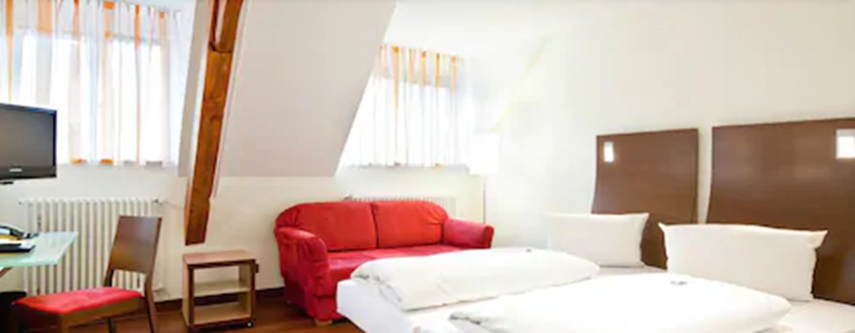 A hotel room with a bed, a red sofa, a TV, and a small table.