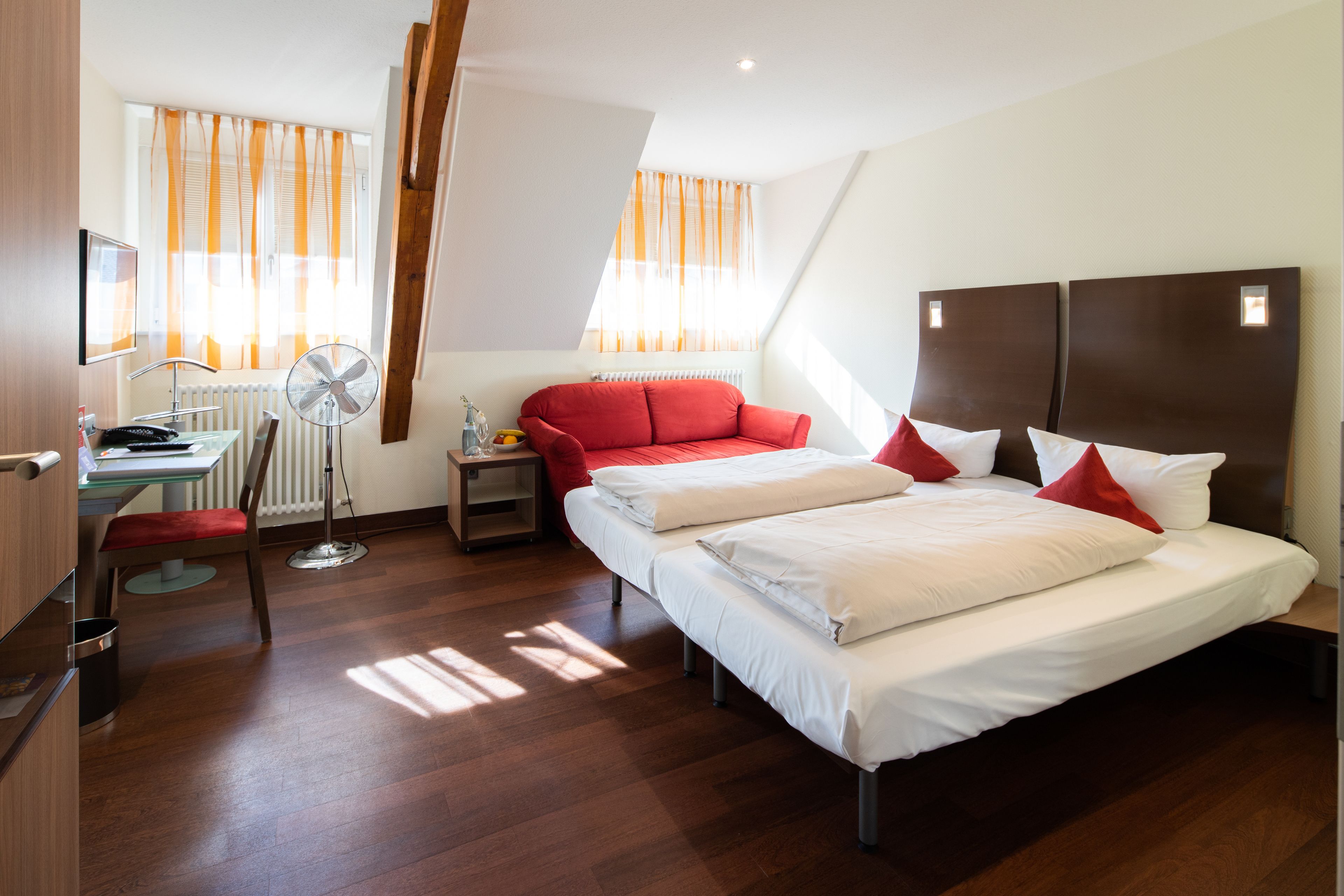 Une chambre d’hôtel avec un grand lit, un bureau avec une chaise, un canapé rouge et une fenêtre avec des rideaux.