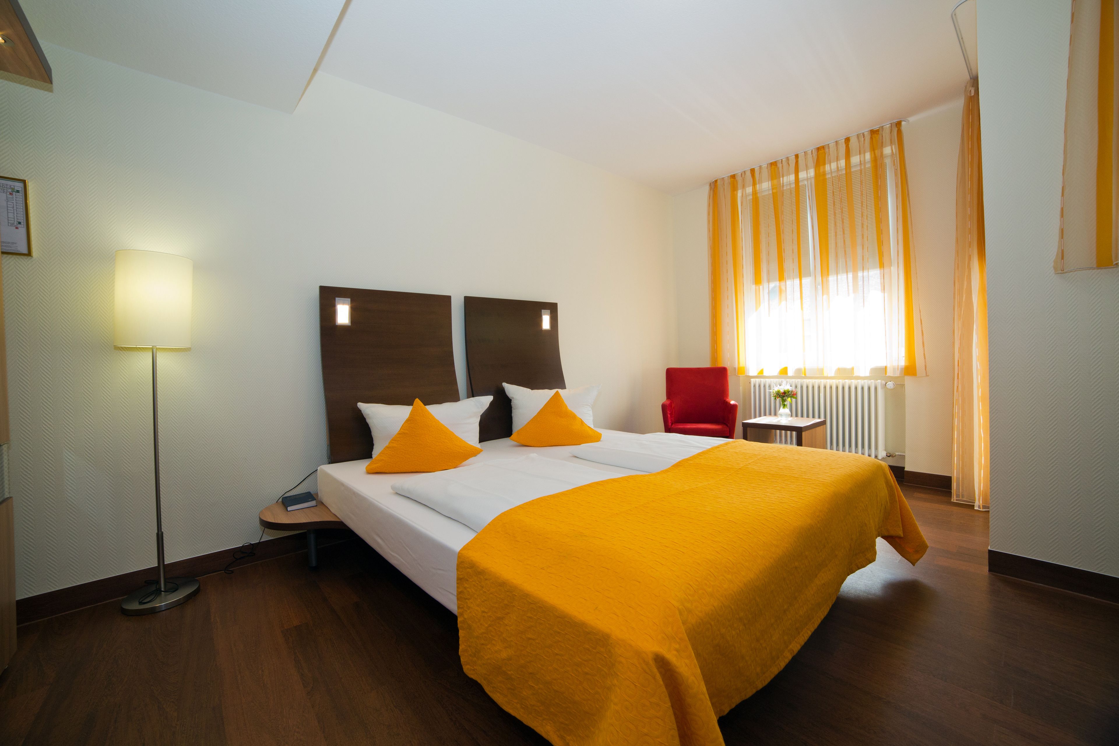 A hotel room with a bed, a desk, a chair, and a lamp.