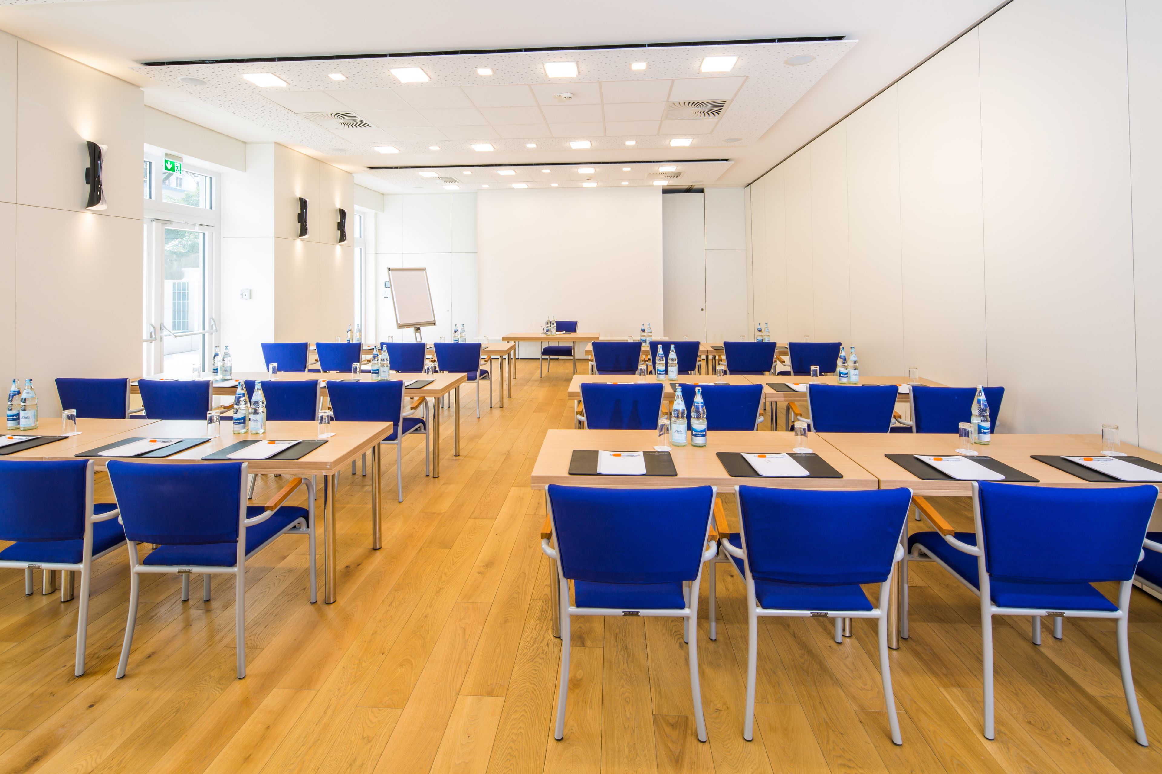 A conference room with multiple tables and blue chairs, equipped with water bottles and nameplates.