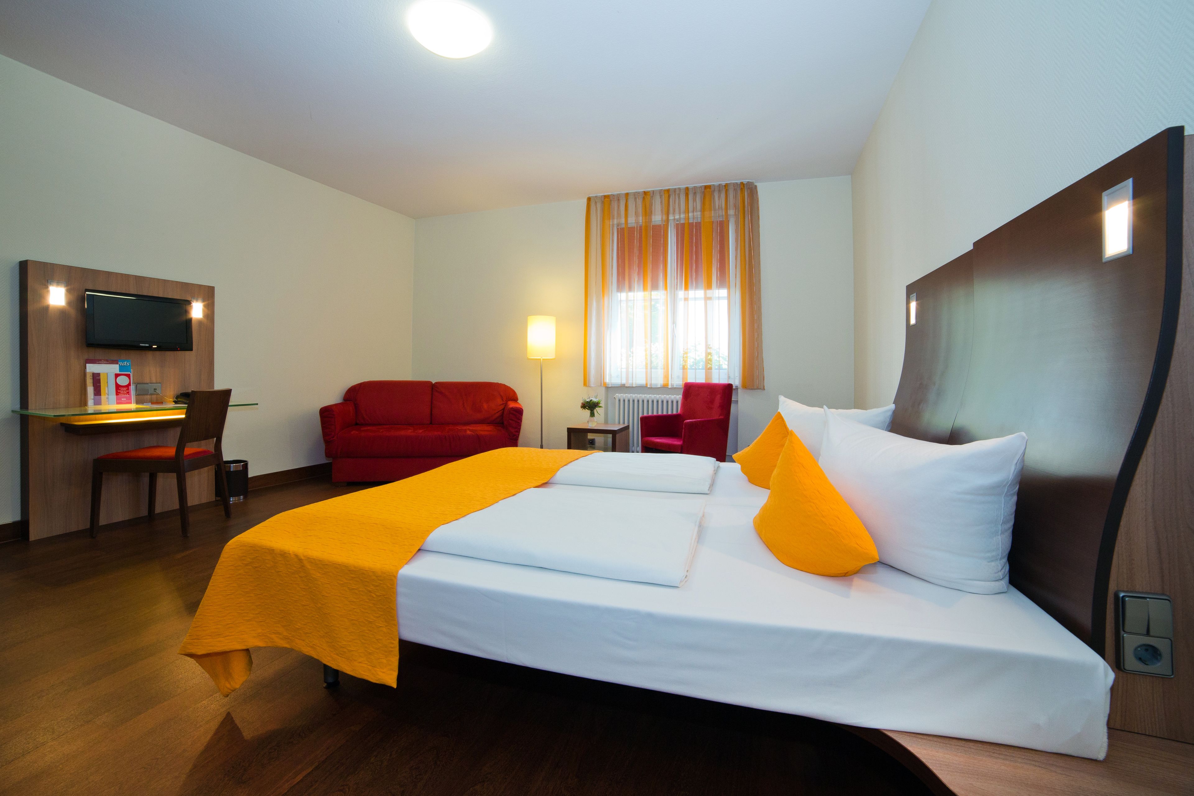 Ein Hotelzimmer mit Bett, Schreibtisch, Stuhl, Fernseher und einem Fenster mit Vorhängen.