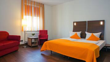 Ein Hotelzimmer mit einem großen Bett, einem roten Sessel, einem kleinen Tisch und einem Fenster mit Vorhängen.