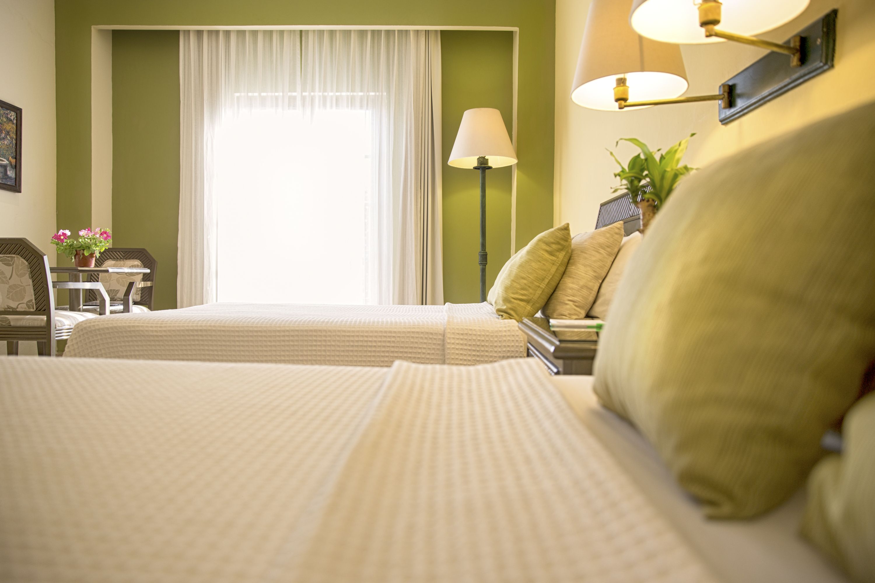 Ein Hotelzimmer mit zwei Betten, einem Schreibtisch mit Stuhl, einer Lampe und einem Fenster mit Vorhängen.