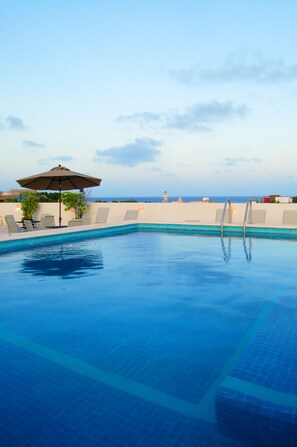 A swimming pool with a view of the ocean, lounge chairs, and an umbrella. - Hotel Los Itzaes by 5th av (Playa del Carmen)
