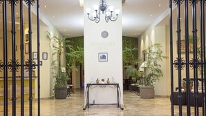 Un vestíbulo de hotel con un mostrador de recepción, una araña de cristal y plantas en macetas.