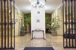 A hotel lobby with a reception desk, a chandelier, and potted plants.