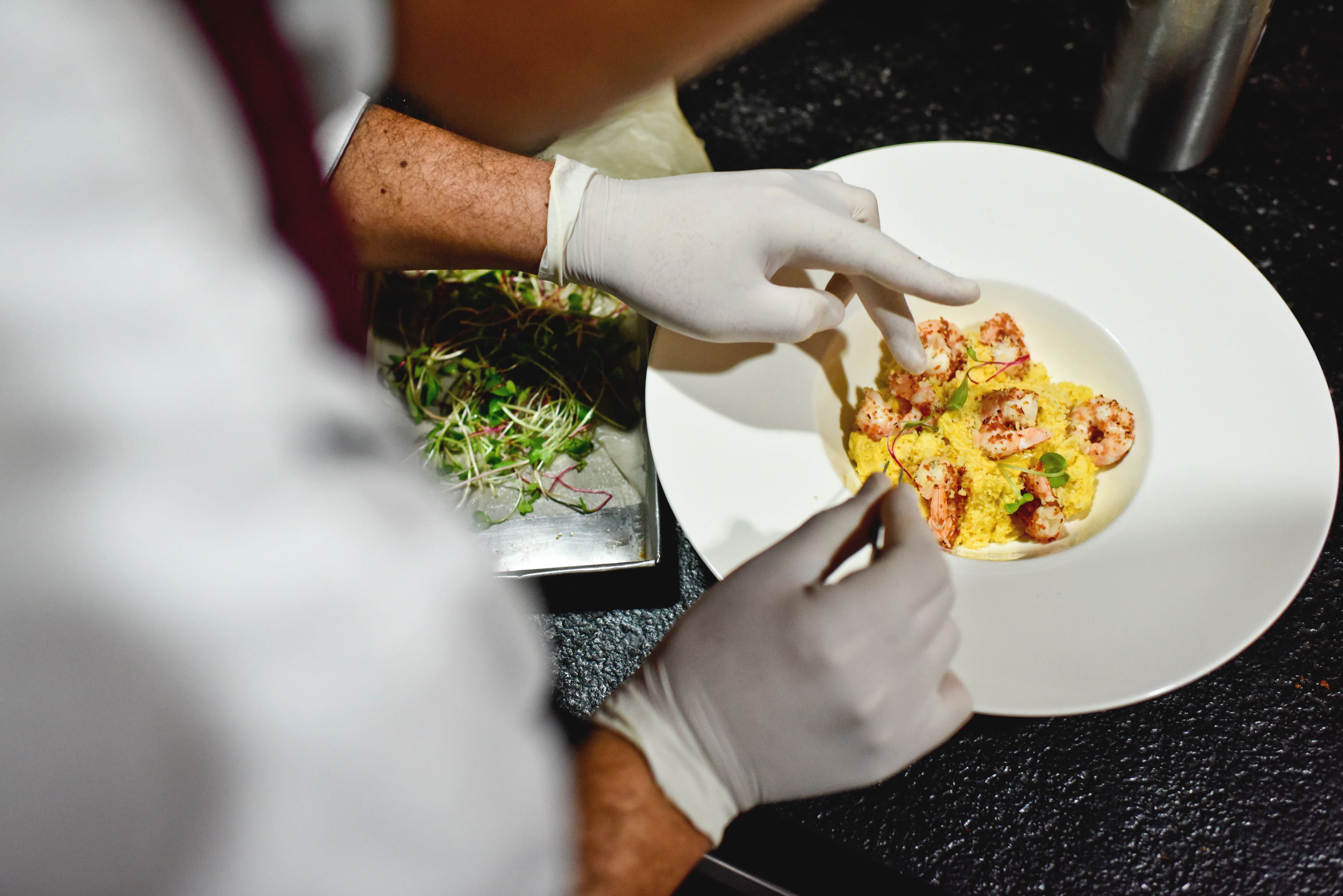 A person wearing gloves preparing a dish on a white plate.