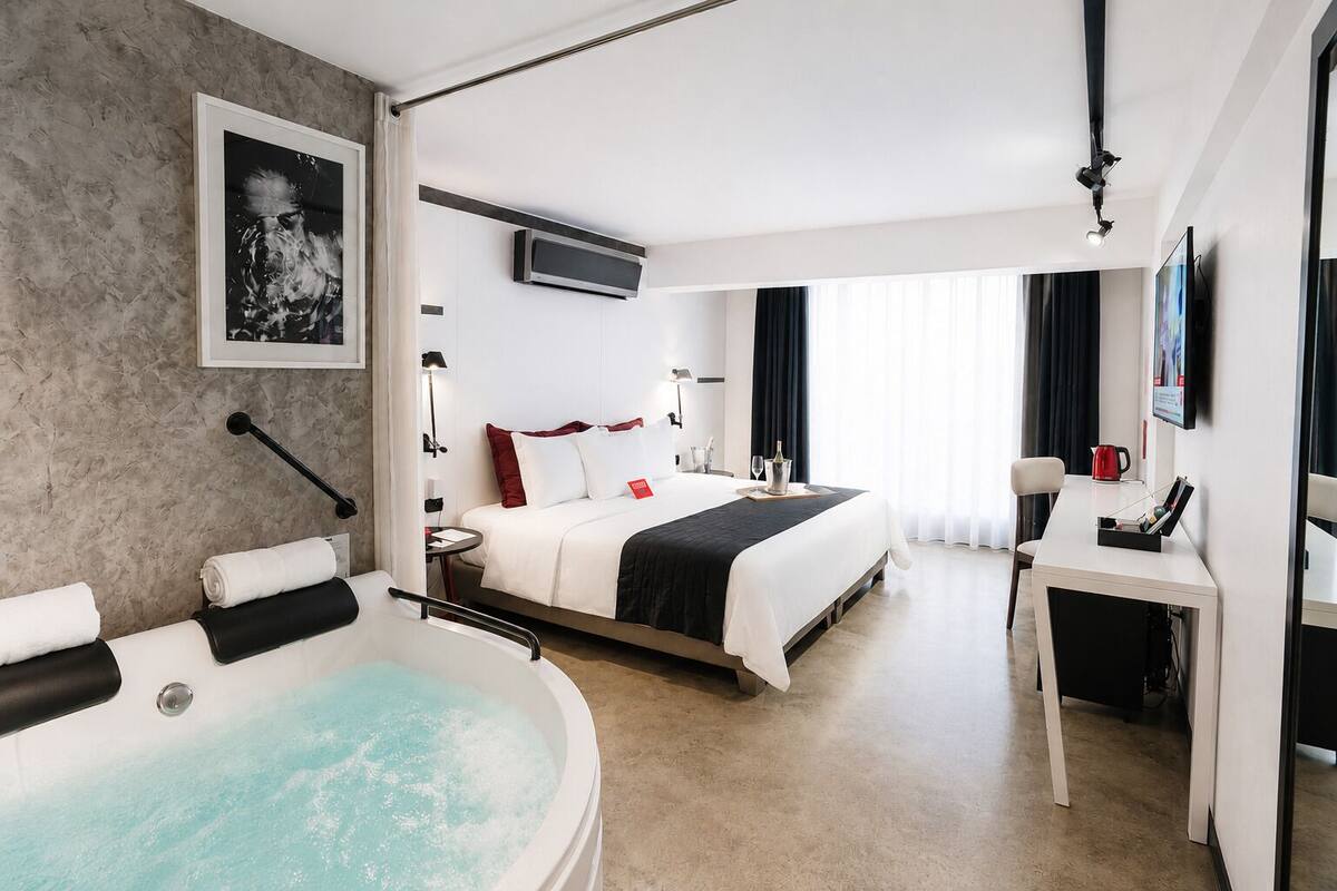 Una habitación de hotel moderna con una cama grande, un escritorio independiente, una bañera y un televisor de pantalla plana.