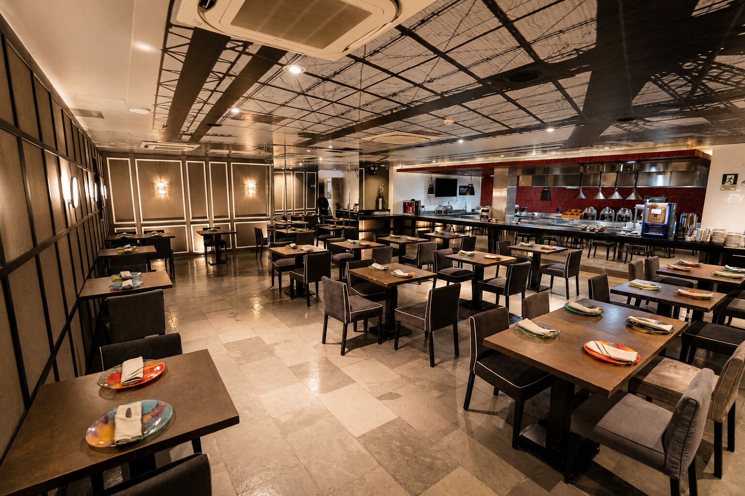 A spacious restaurant with multiple tables and chairs, a kitchen area, and a high ceiling with exposed beams.