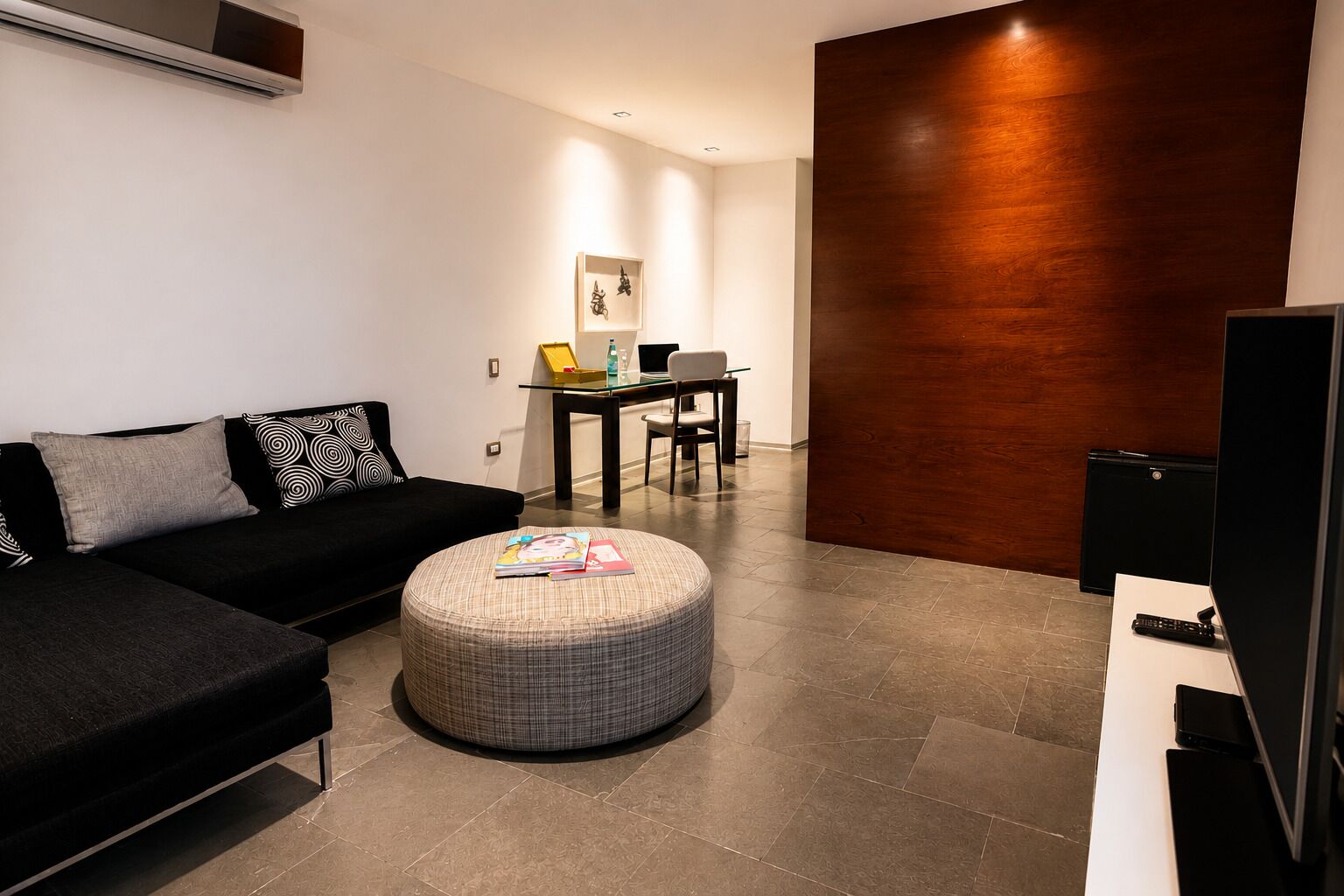 A modern living room with a sofa, ottoman, and a flat-screen TV.