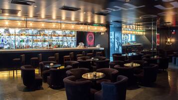 Uma área de bar com uma seleção variada de bebidas, diversos arranjos de assentos e um design de interiores moderno.