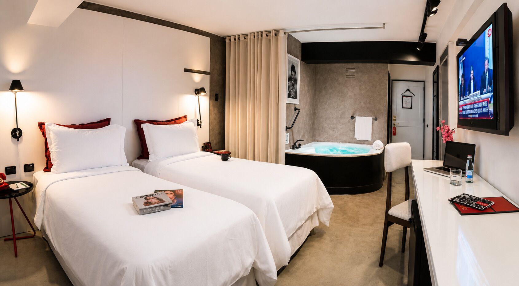 A hotel room with two beds, a desk, a TV, a shower, and a bathtub.