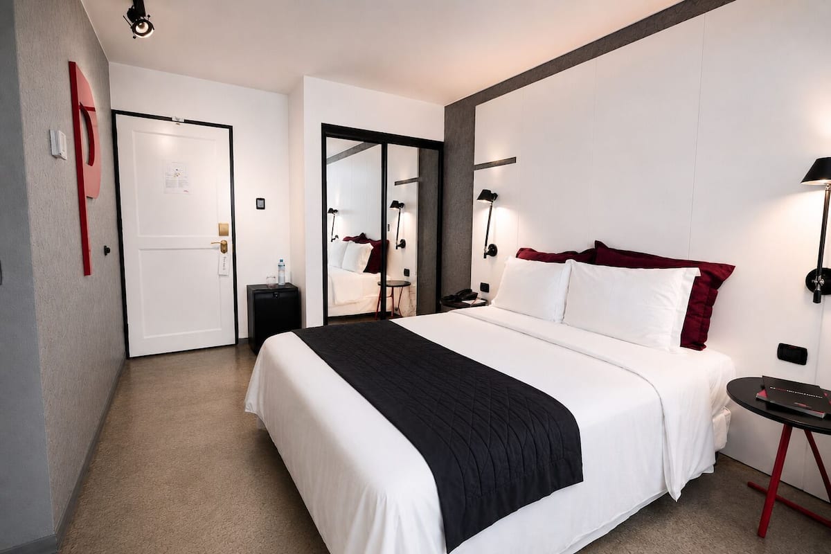 Una habitación de hotel moderna con una cama grande, mesitas de noche, un escritorio y un espejo.