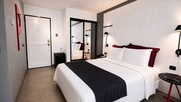 Una habitación de hotel moderna con una cama grande, mesitas de noche, un escritorio y un espejo.
