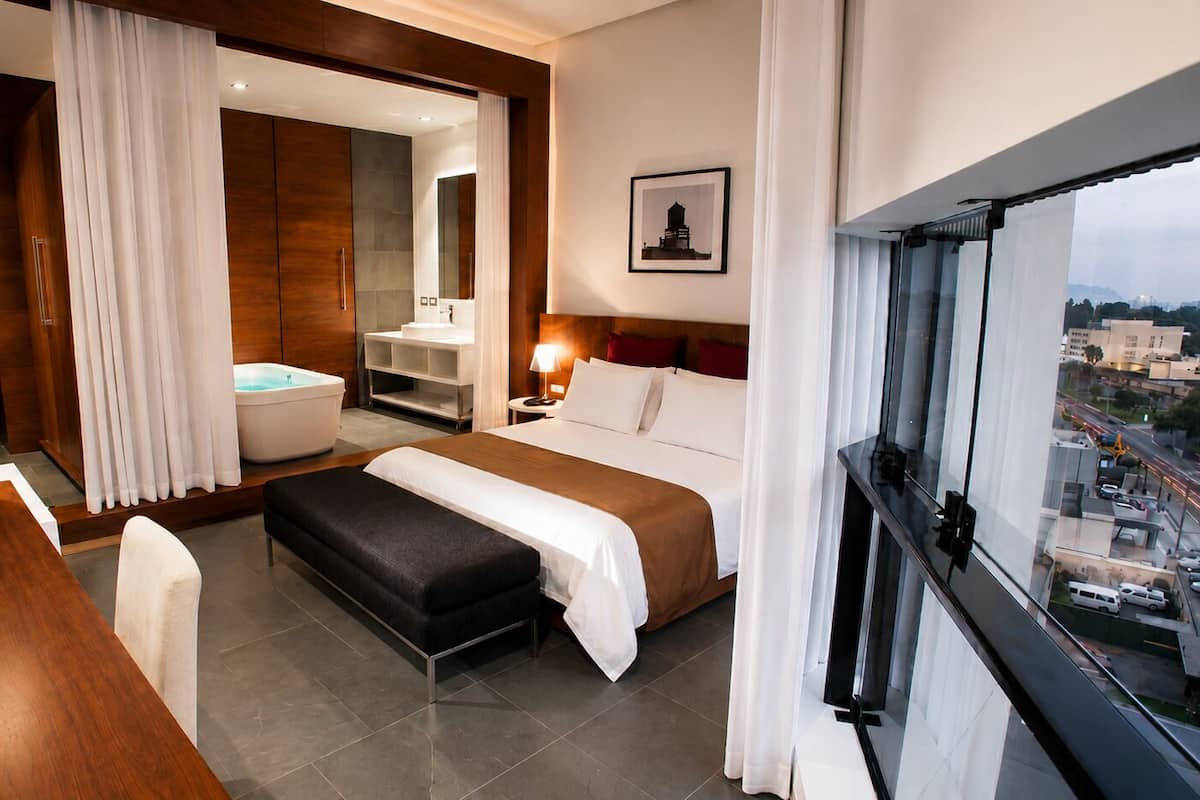 Una habitación de hotel moderna con cama, escritorio, televisión, baño con bañera y vista a la ciudad.