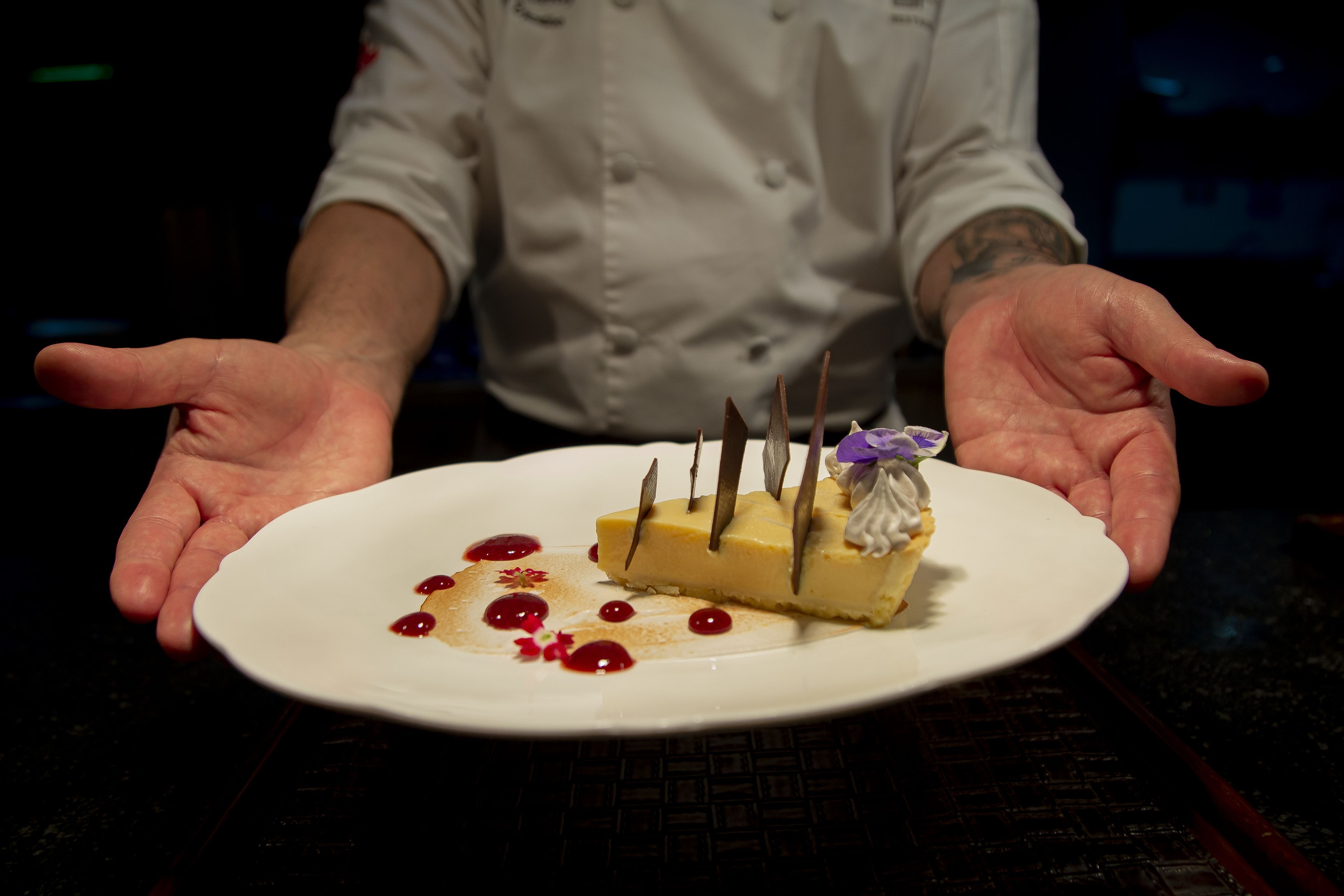 A dessert on a white plate with a person’s hands extended towards it.