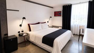 Een hotelkamer met een bed, nachtkastjes, een bureau, een stoel en een raam met gordijnen.