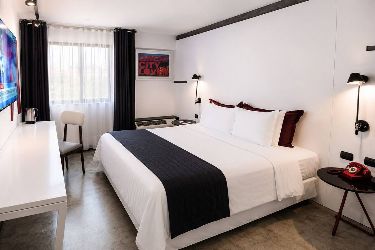 Una habitación de hotel con cama, escritorio, silla, televisor y una mesita con teléfono.