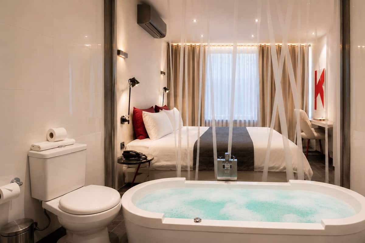 Un baño moderno con bañera, inodoro y una cama con cortinas.
