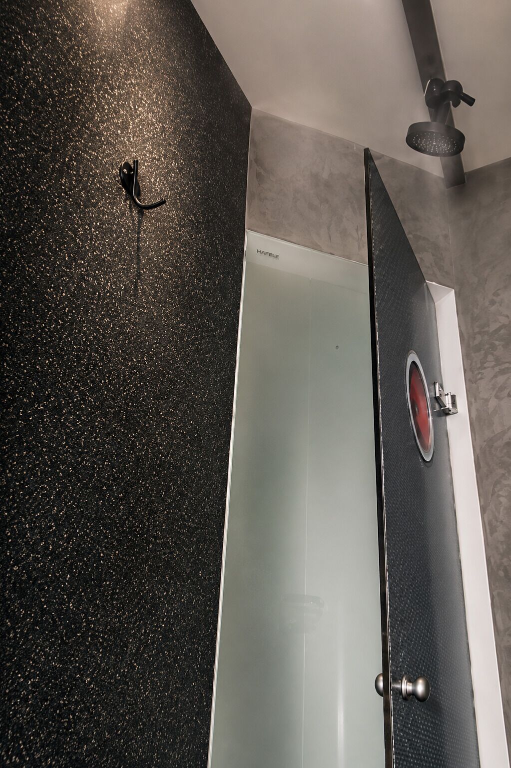 A bathroom with a black speckled floor, a white bathtub, and a shower area with a control panel.