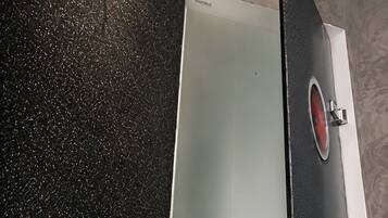 A bathroom with a black speckled floor, a white bathtub, and a shower area with a control panel.