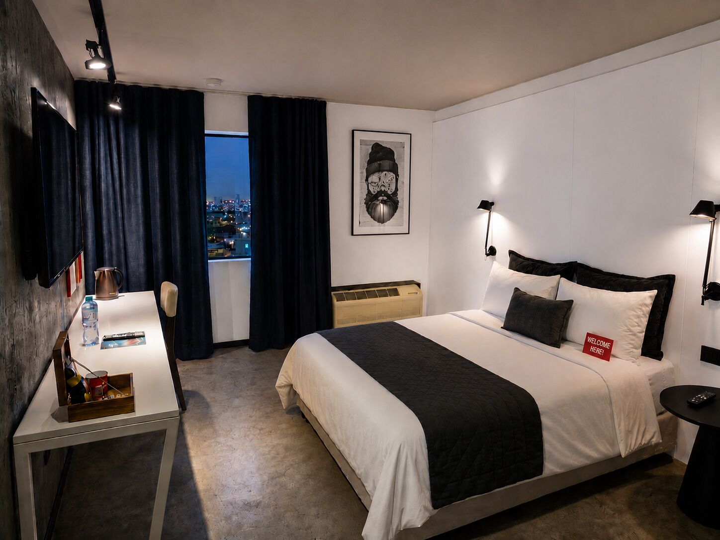 A hotel room with a bed, bedside tables, a desk, a chair, a window with curtains, a city view, and a framed picture on the wall.
