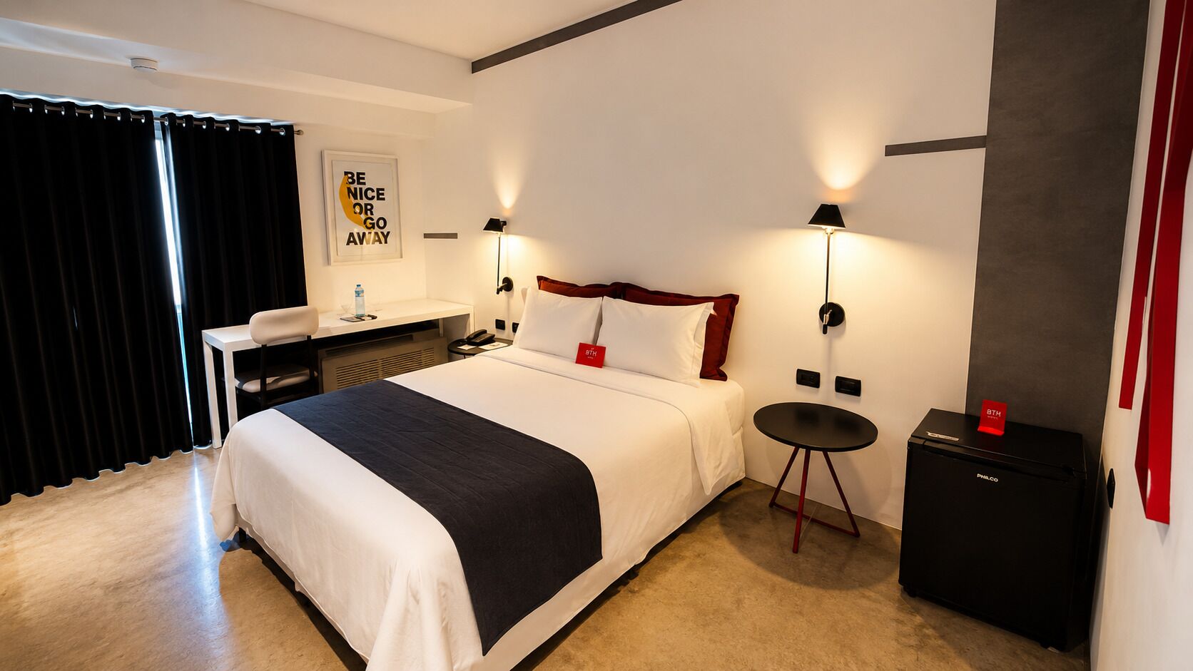 A hotel room with a bed, bedside table, lamp, and a small black cabinet.