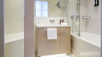 Un baño moderno con cabina de ducha de vidrio, un lavabo blanco y un tocador color beige.