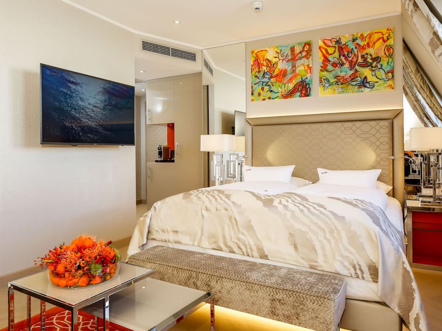 Quarto de hotel moderno com uma cama grande, televisão, escrivaninha e uma obra de arte vibrante na parede.