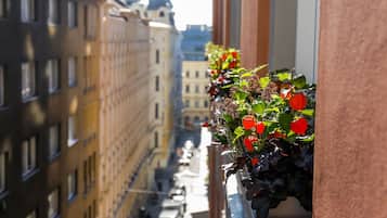 A narrow street with buildings on either side, a balcony with red flowers, and a clear view of the street.