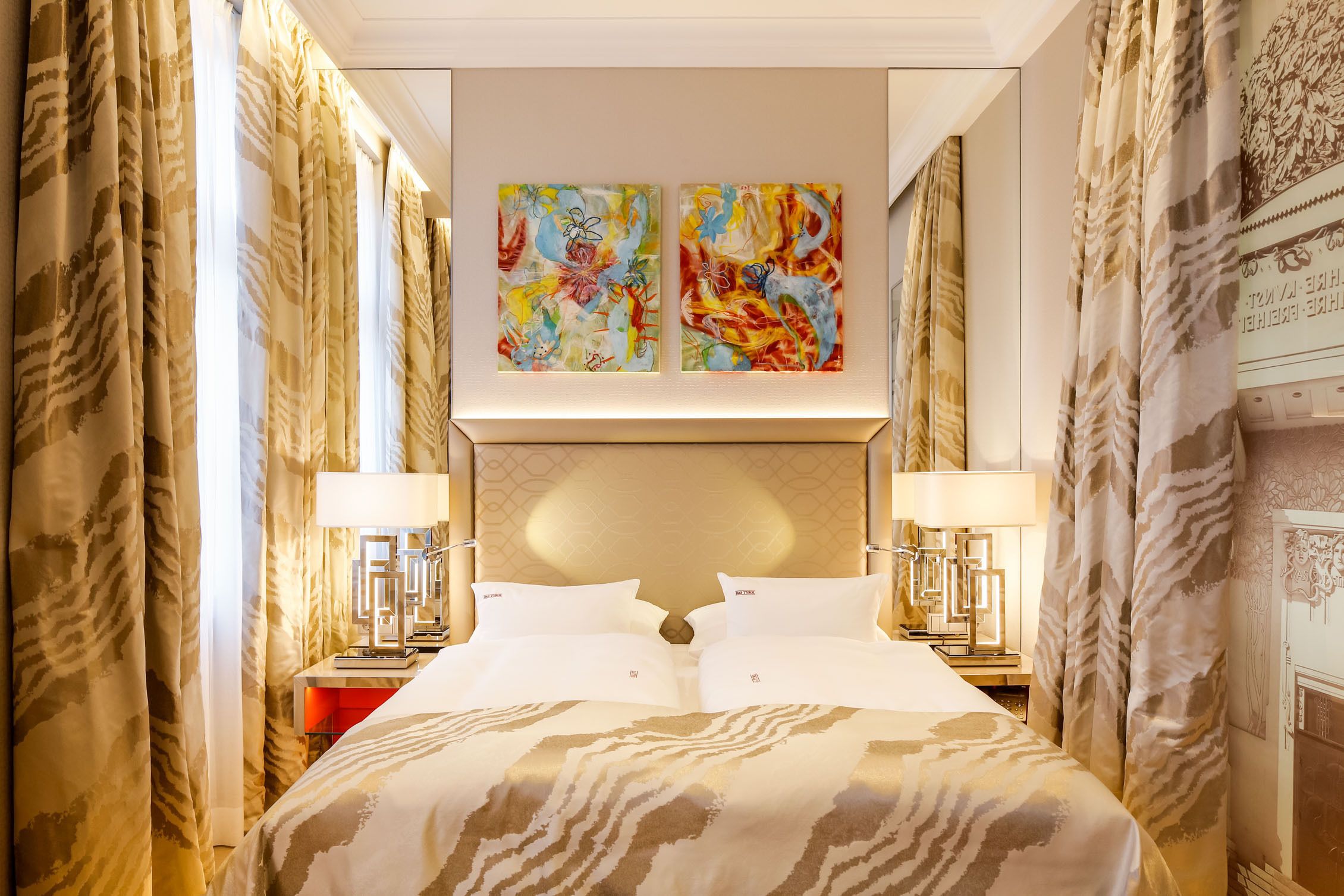 A hotel room with a large bed, two bedside tables with lamps, and two abstract paintings on the wall.