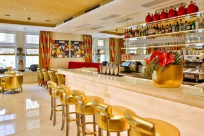 A bar area with golden chairs, a counter, and a shelf with bottles and glasses.