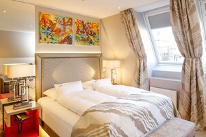 Quarto de hotel com uma cama grande, mesas de cabeceira com luminárias, telefone e janela com cortinas.