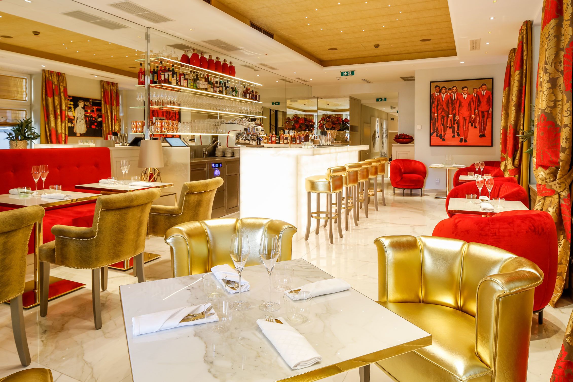 A restaurant with red and gold decor, marble tables, and gold chairs.