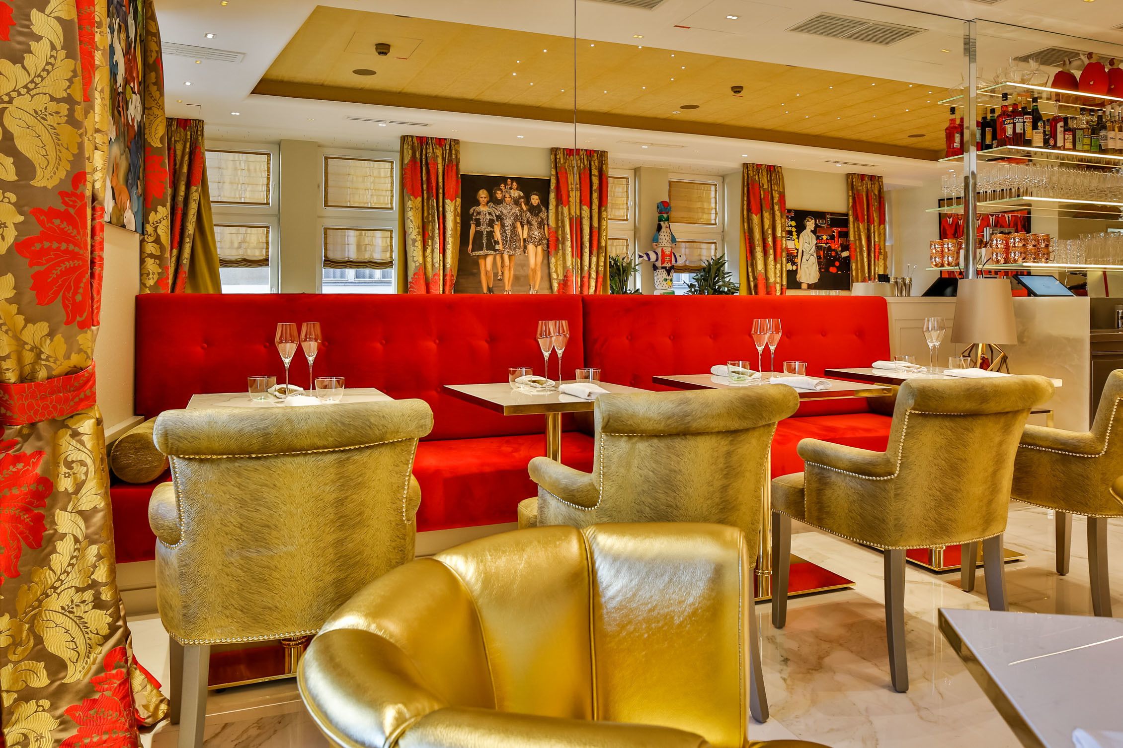 Un restaurante con asientos rojos, sillas doradas y una zona de bar con estanterías llenas de copas y botellas.