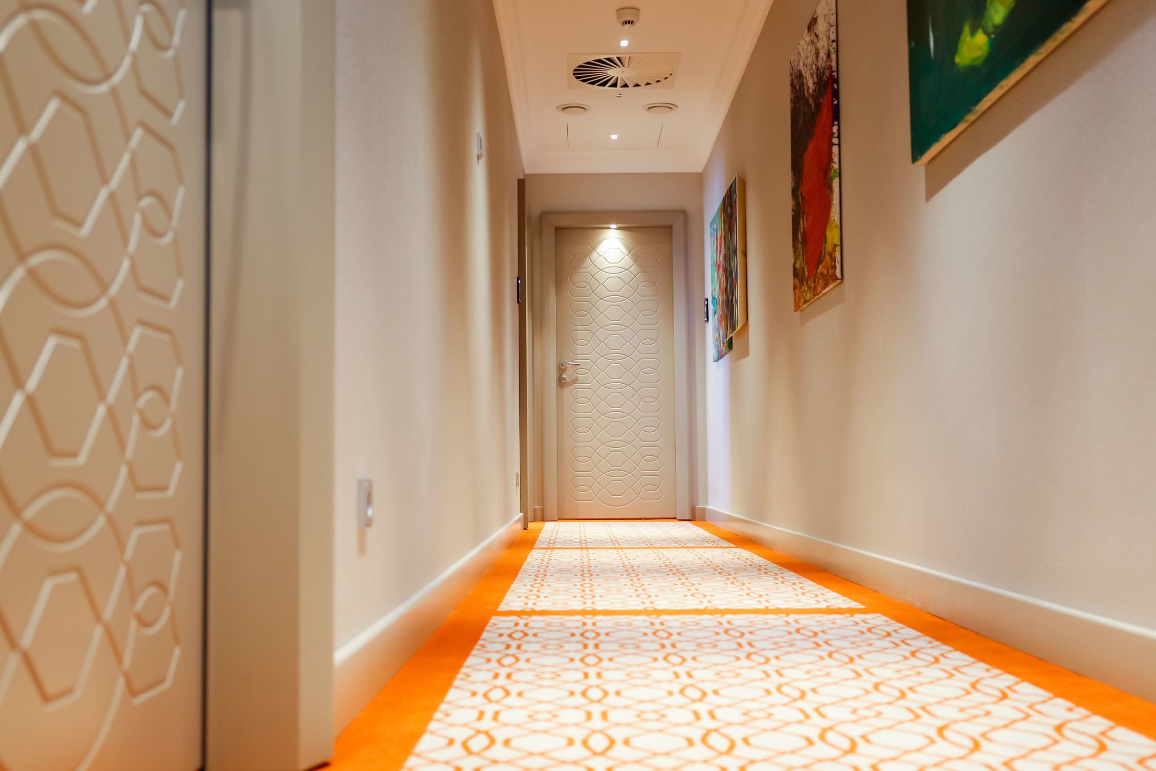 Un pasillo con alfombra estampada, una puerta con diseño geométrico y una lámpara en el techo.