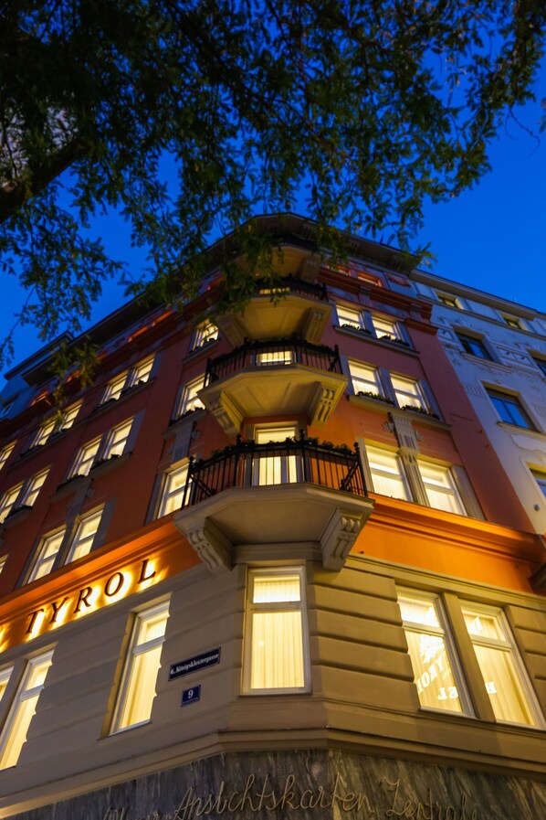 Un edificio de varios pisos con ventanas e balcones iluminados, que muestra el nombre