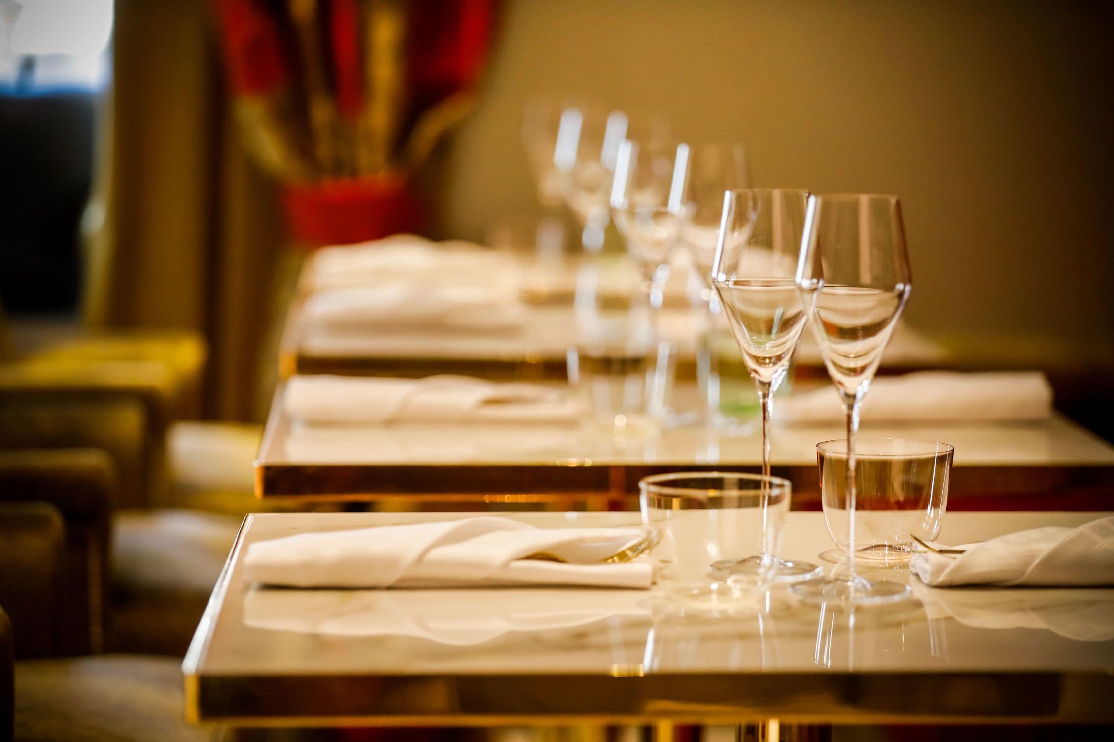 A row of tables with wine glasses and water glasses, neatly arranged with white napkins.