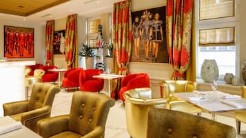 Un vestíbulo de hotel con sillas rojas y doradas, un mostrador de recepción de mármol y cuadros grandes enmarcados en las paredes.