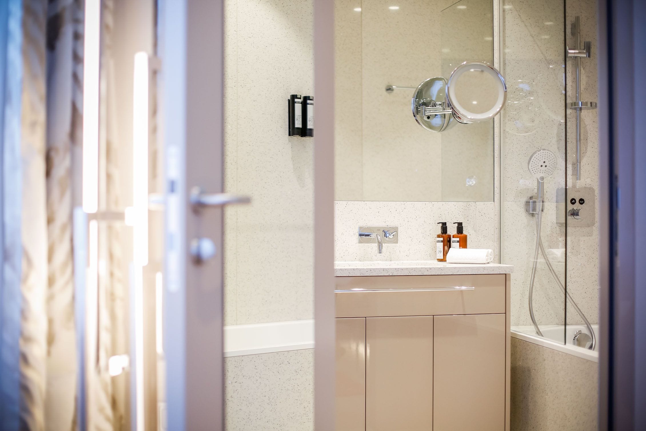 A modern bathroom with a glass shower enclosure, a beige vanity, and a mirror above the sink.