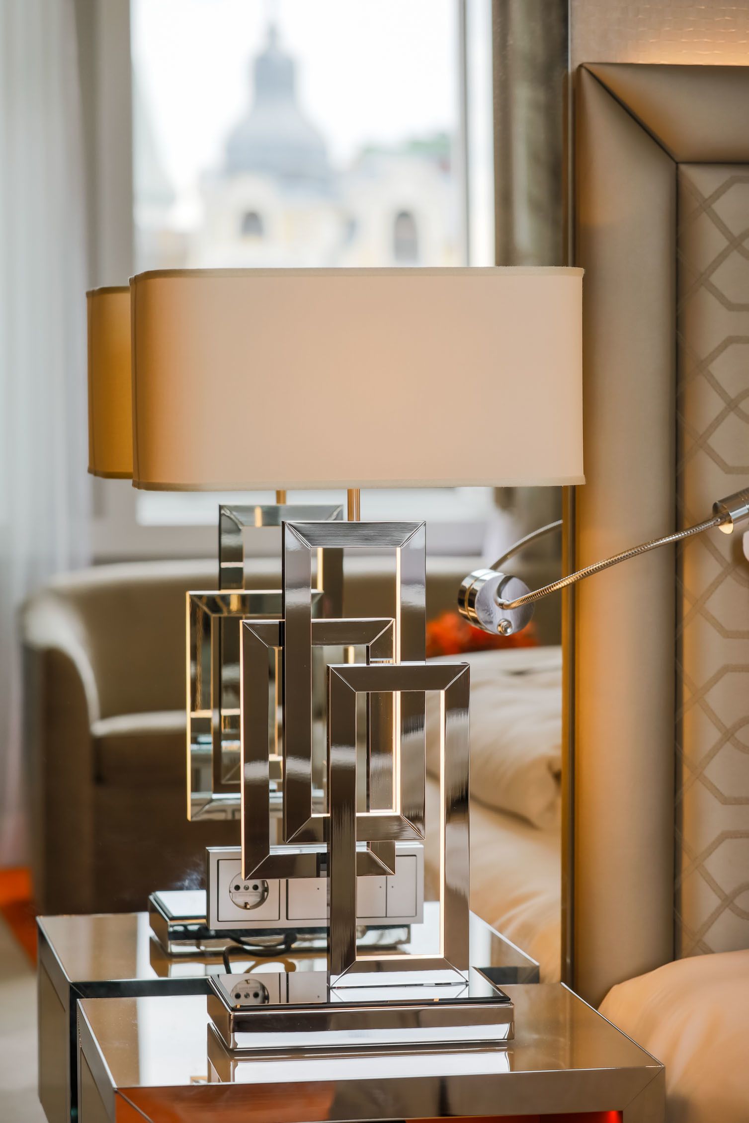 Eine moderne Lampe mit geometrischem Design auf einem Nachttisch in einem Hotelzimmer.