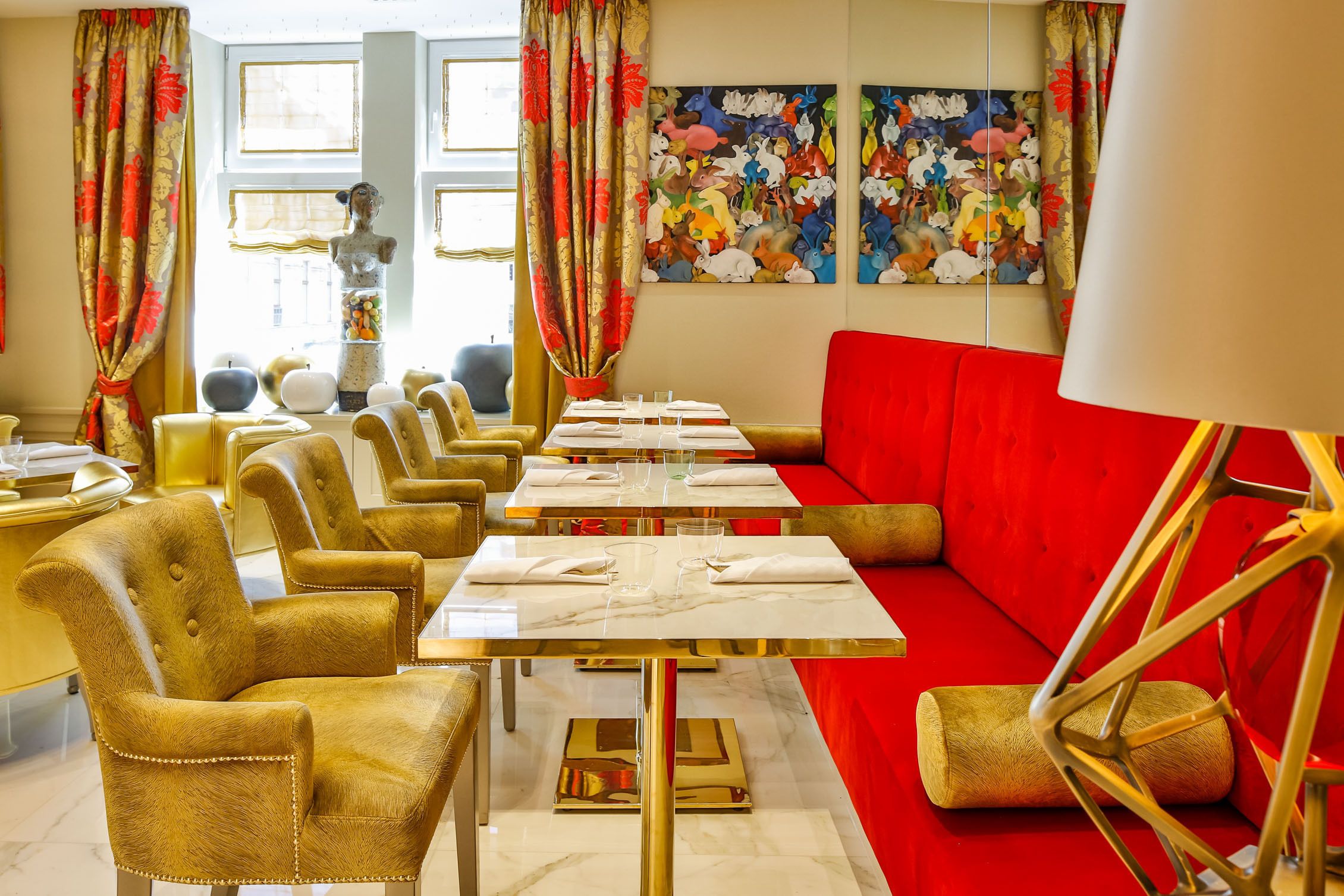 A dining area with gold chairs, red sofas, and a marble table set for dining.